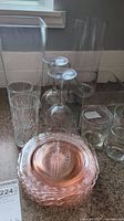 Clear glassware including two large rectangular vases, stem glasses, tumblers, and pink colored glass plates on a counter.