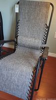 Full view of folding gravity chair showing the gray woven fabric, metal frame, and attached headrest pillow.