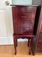 Front view of wooden jewellery cabinet showing the four drawers and two side doors with decorative handles and carved legs.