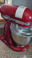 Full view of red mixer on countertop with metal bowl and power cord