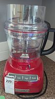 Red KitchenAid food processor base with clear processing bowl and lid, showing control panel with Low, High, Pulse buttons and thickness adjustment slider.