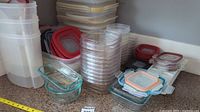 Wide view of many stacked clear plastic containers with various lids, some with red seals, and several glass containers with lids