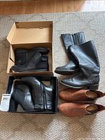 Four pairs of ladies boots and shoes arranged on floor and in box, showing style and color variety
