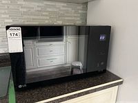 Front view of black LG microwave oven showing reflective glass door and digital clock display at 12:32.