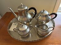 Pewter tea set arranged on tray: coffee pot, tea pot, creamer, sugar bowl with lid and side handles, all with traditional shape and black wrapped handles on pots.