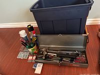Overview of tools including metal Craftsman toolbox open with hand tools inside and Rubbermaid bin behind it containing additional tools and supplies.