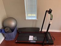 Photo of treadmill folded with treadmill belt, control area, manual, and safety cord visible alongside exercise accessories.