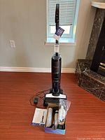 Front view of assembled Tineco Floor One unit on charging station with accessories box on floor.