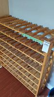 Front angled view of wooden wine rack showing slatted shelves and dimensions on green tape: W 33" D 10.5" H 37".