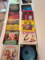 Photo showing 12 vinyl record covers laid out on a white surface. Includes children's albums like Strawberry Shortcake and Cinderella, the E.T. picture disc, The Carpenters Collection, a Duran Duran album, Broadway Hollywood, and Saturday Night Fever soundtrack.