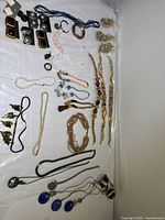 Top view of assorted vintage and costume jewelry including necklaces, earrings, brooches, and bags of beads on white backdrop.