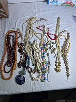 Top down view of assorted vintage costume jewelry necklaces on a white background showing various colors, bead styles and pendants.