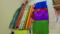 Gift wrapping paper rolls and some large gift bags in various colors including red, blue, purple, and green on a table.