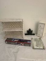 All five items displayed together on white backdrop: white wicker wall shelf with three tiers, small white wooden three-drawer chest, black maple leaf wall hook, mirrored vanity tray with gold corners, and boxed telescoping tie rack