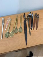 Photo of assorted letter openers laid on a wooden surface, showing variety of handles including tennis rackets and other metal handle designs