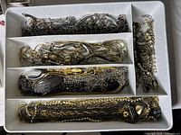 Image of assorted necklaces coiled in white compartmentalized container showing different metallic tones, including silver and gold. Some include beads and pendants.