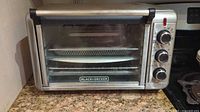 Front view of Black & Decker air fryer toaster oven combo on kitchen counter, showing stainless steel body, glass door with black trim, and control knobs on right side.