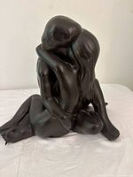 Front-side view of ceramic lovers sculpture showing seated couple embracing with dark bronze/black finish.