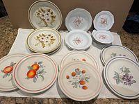 Overall display of decorative and dinner plates and bowls with various fruit and floral motifs, showing pattern variety and condition.