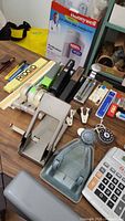 Photo showing a variety of vintage and modern office supplies including staplers, rulers, tape dispensers, punches, and calculators.