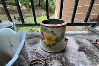 Cylindrical ceramic flower pot with painted colorful flowers placed on outdoor surface