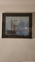 Full view of the framed sailboat art print showing a realistic nautical scene against a misty city skyline background, with reflections on the glass.