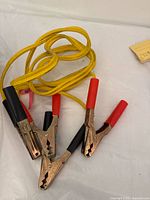Yellow jumper cables with red and black clamps laid out in loosely coiled state showing clamp details and cable condition.