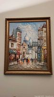 Full view of framed impressionist oil painting showing cityscape with street, buildings, dome, and figures under an overcast sky.