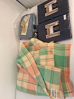 Photo showing the folded pastel plaid Invicta wool blanket alongside folded packaged navy blue drapery panel and the blue queen sheet set.