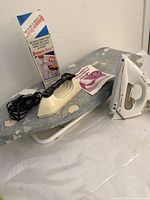 Electric iron, portable steamer, ironing board with floral cover, manuals, cords, and original box of the steamer