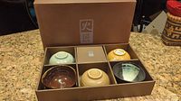 Top view of six Japanese rice bowls arranged in original brown box with dividers