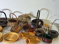 Image showing a variety of wicker baskets including rustic twig baskets, a lidded hut-style basket, colorful handwoven baskets with fabric lining, and different sizes of woven trays and serving baskets.