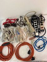 Image showing assortment of power strips, extension cords in various colors including orange, blue, white, coiled red cords, and plug adapters.