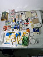 Top-down photo of assorted hardware and electrical supplies spread on a white surface, items include outlet covers, switches, wire connectors, and various packaging.