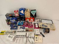 Wide view of lighting and electrical hardware lot including boxed Philips and GE light bulbs, switch plates, wiring spools, and Address Light Kit box