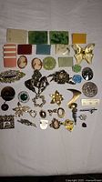 Lot of over 30 costume brooches and pins including enamel, metal, resin pieces in various shapes and colors, laid out on a white fabric background