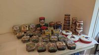 Overall view of 40+ assorted decorative gift tins in various shapes and themes on a table.