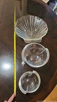 Top down and side view showing two round clear lead crystal bowls and two clam shell shaped glass bowls arranged on a wooden table with measuring tape for scale.