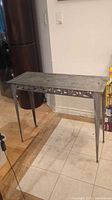 Full view of the metal console table showing the rectangular top with geometric patterned edges and four tapered legs.