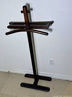 Full view of the wooden valet stand showing the base, central vertical support, pants bar, jacket hanger, and accessory tray