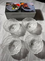Four frosted glass salad bowls set arranged in front of Mikasa Crystal box, showing the bowls from top view with leaf and berry pattern.