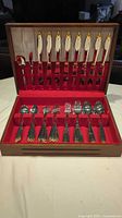 Full view of Mikasa flatware set in red velvet-lined wooden case showing knives, forks, spoons, and serving utensils arranged in slots.
