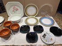 Variety of decorative and vintage plates and saucers arranged on table, showing different materials and styles.