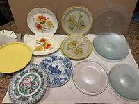 Lot showing variety of ceramic, porcelain, and glass plates with floral and patterned designs, assorted colors and textures.