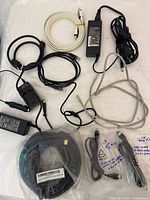 Top view showing assorted cables including two AC power adapters, various HDMI, Ethernet, USB cables loosely arranged on a white background.
