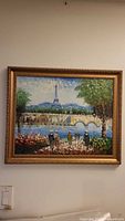 Framed oil painting showing Paris street scene with Eiffel Tower in the background, figures near a waterway and a bridge.