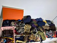 Over 75 assorted scarves and shawls arranged in a container and basket, showing various patterns like animal print, plaid, and floral in diverse colors and sizes.