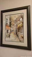 Full view of framed watercolor painting depicting a Paris street scene with people walking and standing, showing buildings with signs and foliage.