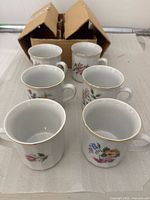 Front view of six porcelain teacups arranged in two rows; showing floral designs and gold trim on rims.