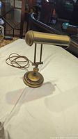 Side view of vintage brass bankers desk lamp with cylinder shade and adjustable arm on a round base.